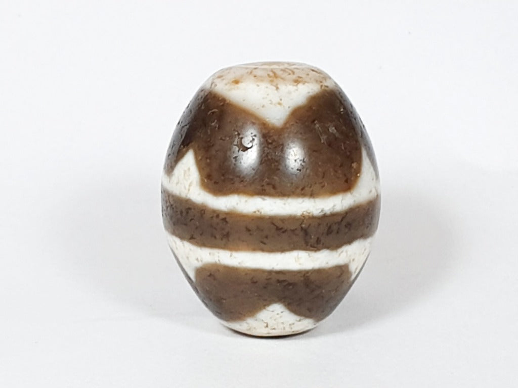 A vintage Dzi bead featuring a round shape with a mesmerizing Tiger Tooth motif. This authentic artifact, identified as R-TT-1, showcases the intricate craftsmanship and spiritual symbolism of ancient Dzi beads