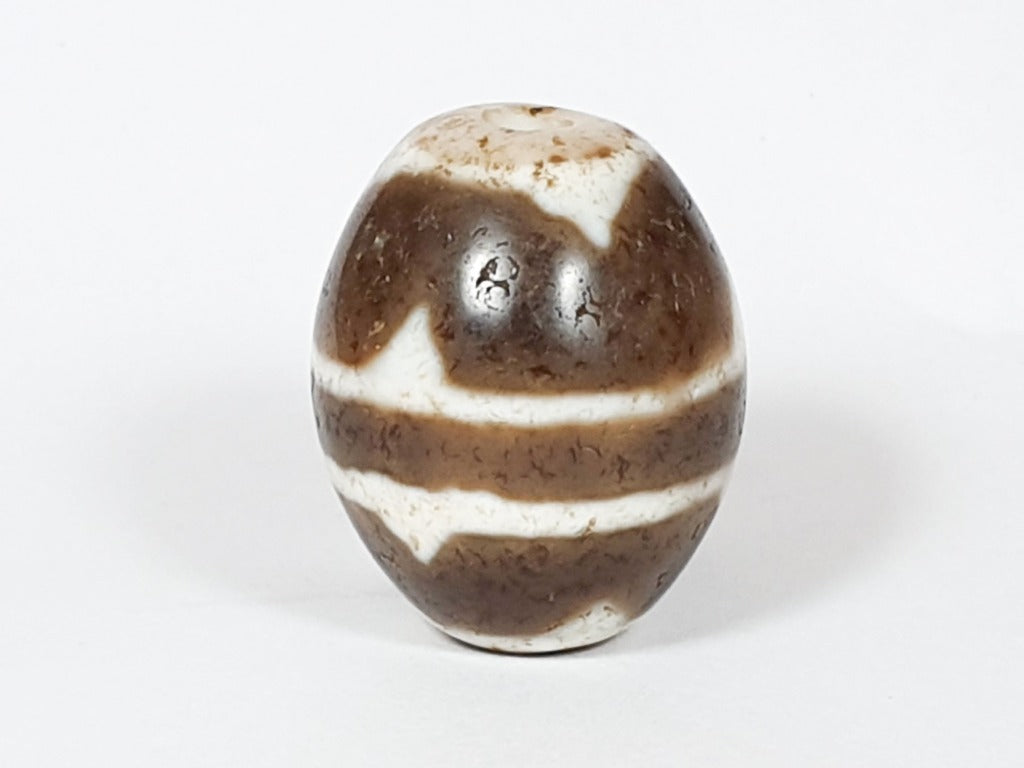 A vintage Dzi bead featuring a round shape with a mesmerizing Tiger Tooth motif. This authentic artifact, identified as R-TT-1, showcases the intricate craftsmanship and spiritual symbolism of ancient Dzi beads