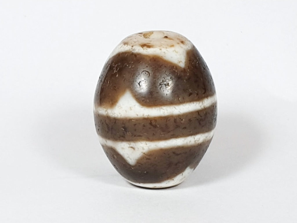 A vintage Dzi bead featuring a round shape with a mesmerizing Tiger Tooth motif. This authentic artifact, identified as R-TT-1, showcases the intricate craftsmanship and spiritual symbolism of ancient Dzi beads