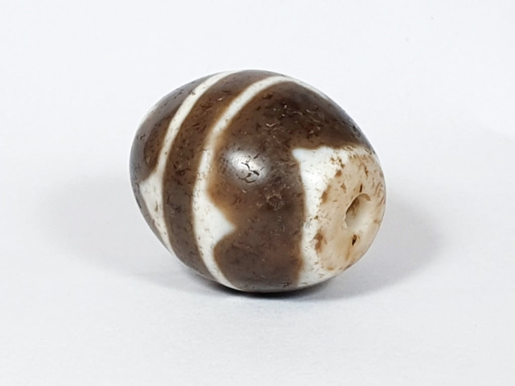 A vintage Dzi bead featuring a round shape with a mesmerizing Tiger Tooth motif. This authentic artifact, identified as R-TT-1, showcases the intricate craftsmanship and spiritual symbolism of ancient Dzi beads