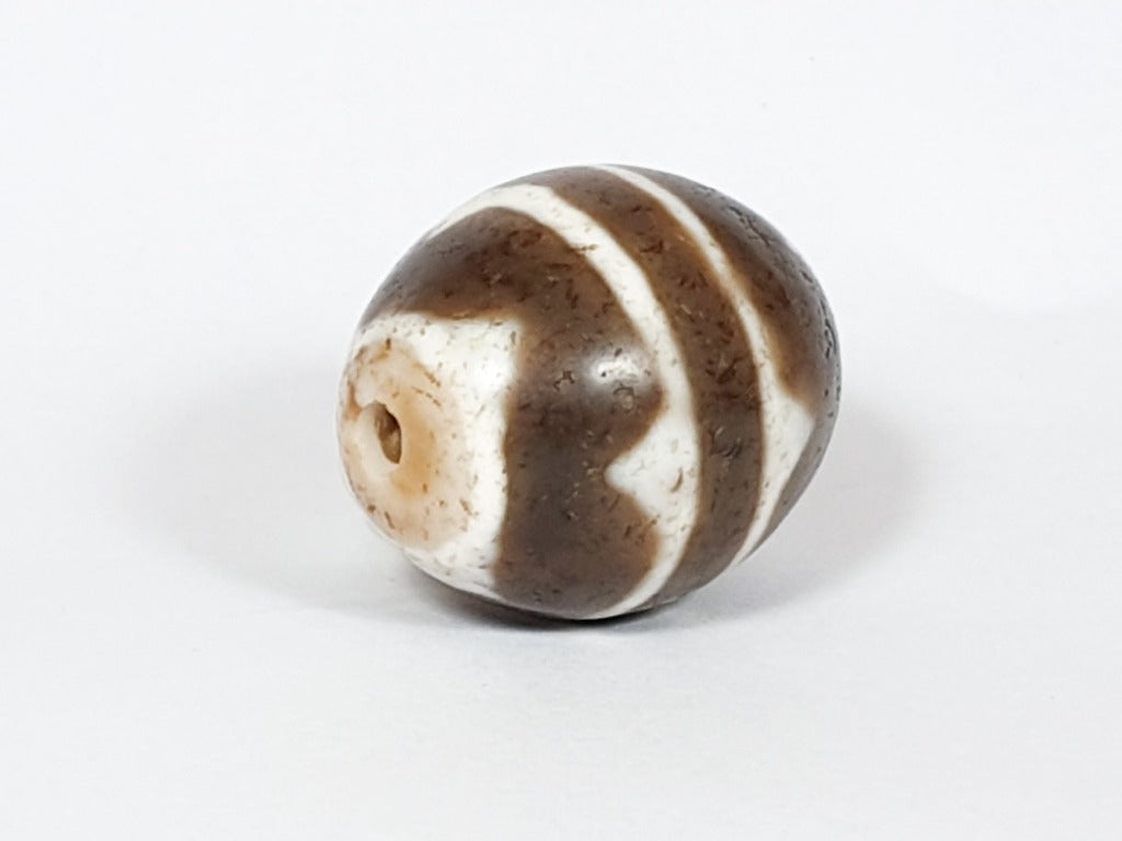 A vintage Dzi bead featuring a round shape with a mesmerizing Tiger Tooth motif. This authentic artifact, identified as R-TT-1, showcases the intricate craftsmanship and spiritual symbolism of ancient Dzi beads