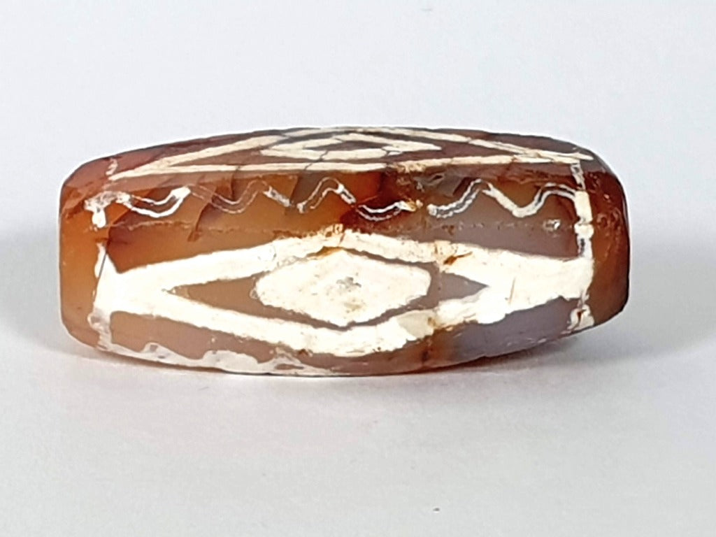  ancient Dzi bead made from Carnelian, showcasing a unique and highly sought-after Four Diamond Eye-In-Eye & Wave motif. This bead is exceptionally rare, adding to its collectability and value. The intricate design combines protective symbolism with the fluidity and power of waves, making it a remarkable piece of ancient craftsmanship and spiritual significance."