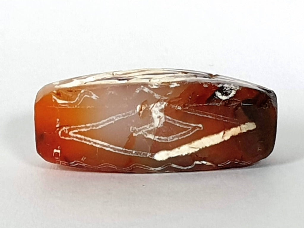  ancient Dzi bead made from Carnelian, showcasing a unique and highly sought-after Four Diamond Eye-In-Eye & Wave motif. This bead is exceptionally rare, adding to its collectability and value. The intricate design combines protective symbolism with the fluidity and power of waves, making it a remarkable piece of ancient craftsmanship and spiritual significance."