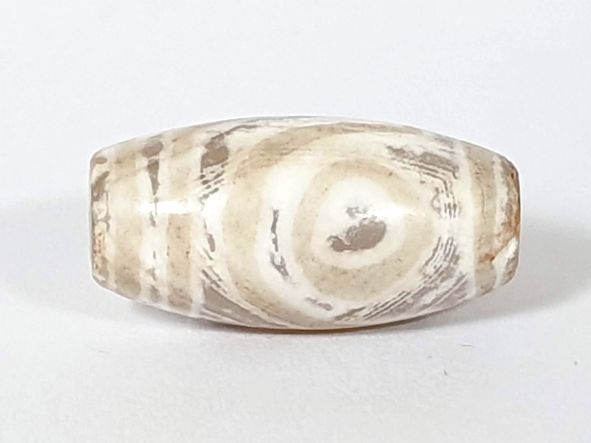 rare white agate dzi bead featuring the two eye motif.  some of the stone's natural patina is visible.  there are also signs of calcification