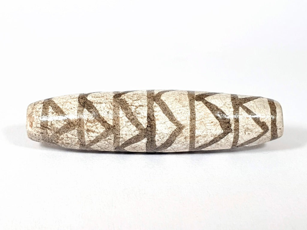 A vintage Dzi bead with a faux antique appearance featuring a captivating white tiger tooth and stripes motif. The bead showcases intricate carvings resembling the patterns found on a tiger's tooth, symbolizing strength, courage, and protection. This unique and beautifully crafted bead is a must-have for collectors and enthusiasts of ancient-inspired jewelry.