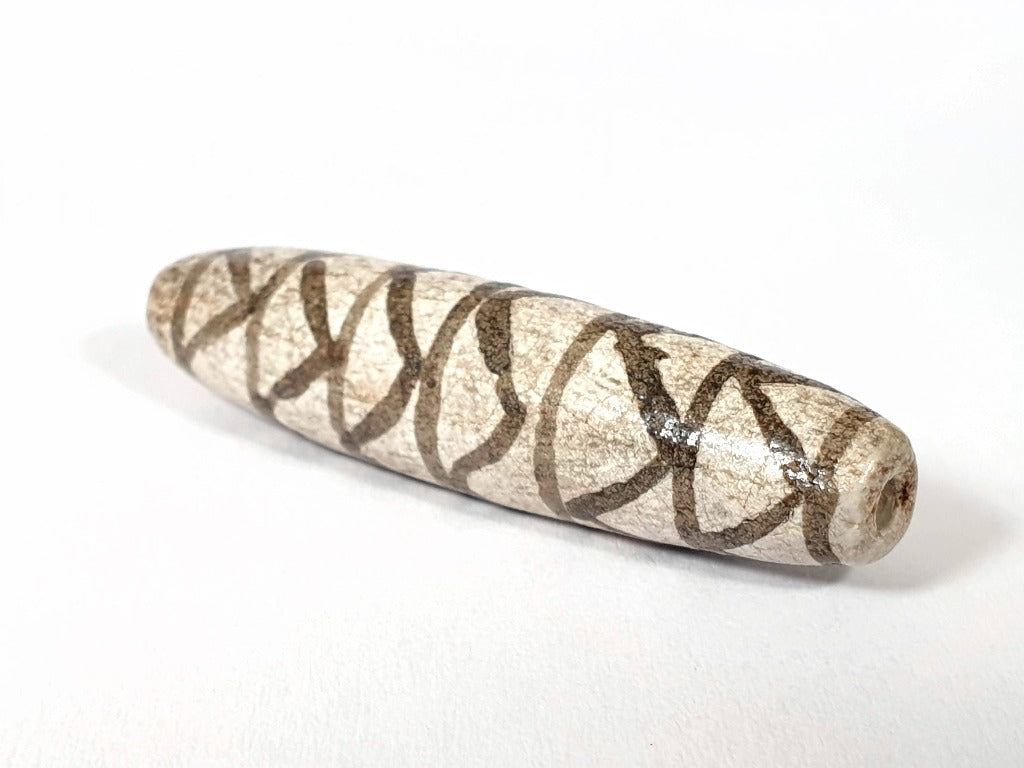 A vintage Dzi bead with a faux antique appearance featuring a captivating white tiger tooth and stripes motif. The bead showcases intricate carvings resembling the patterns found on a tiger's tooth, symbolizing strength, courage, and protection. This unique and beautifully crafted bead is a must-have for collectors and enthusiasts of ancient-inspired jewelry.