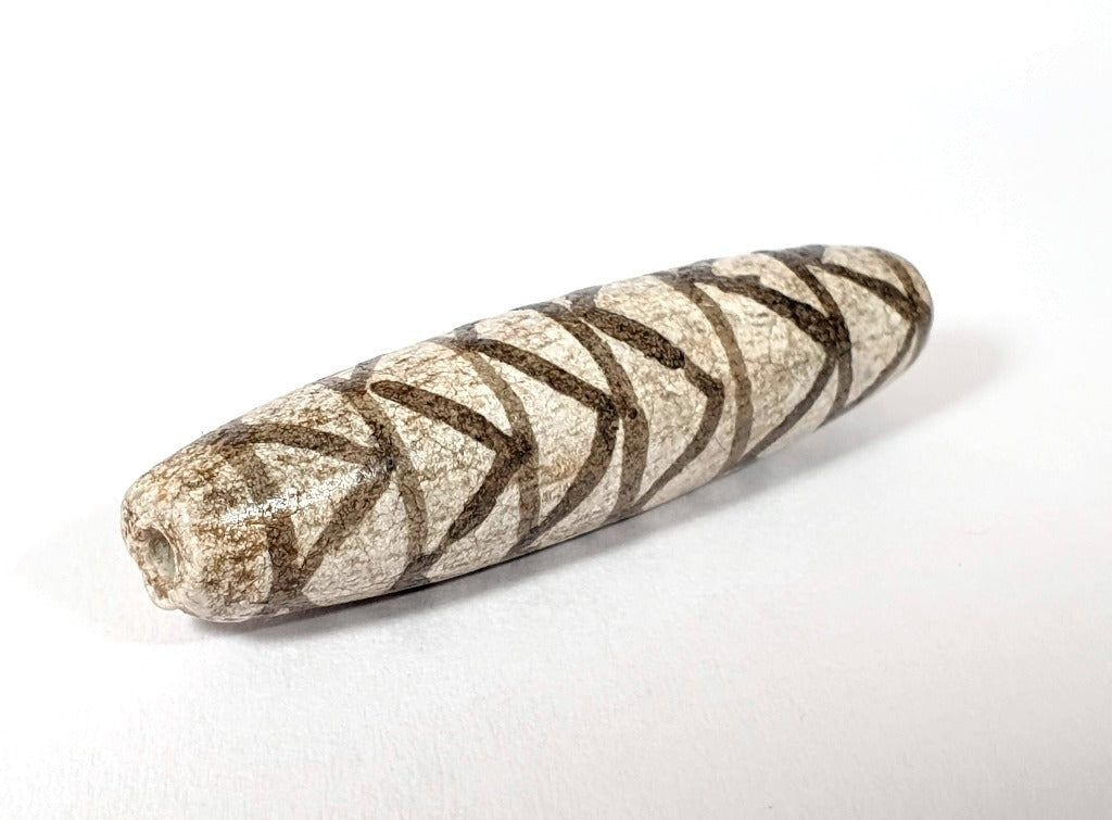 A vintage Dzi bead with a faux antique appearance featuring a captivating white tiger tooth and stripes motif. The bead showcases intricate carvings resembling the patterns found on a tiger's tooth, symbolizing strength, courage, and protection. This unique and beautifully crafted bead is a must-have for collectors and enthusiasts of ancient-inspired jewelry.