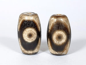  "Pair of New Faux Antique Three Eye Motif Dzi Beads" Description: "A pair of new faux antique Dzi beads with a three eye motif. These beads emulate the look of ancient Dzi beads, offering a stylish and symbolic accessory."