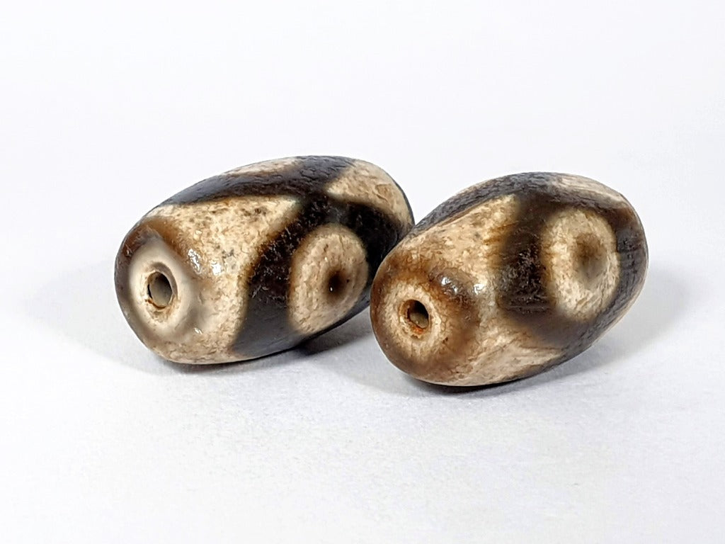  "Pair of New Faux Antique Three Eye Motif Dzi Beads" Description: "A pair of new faux antique Dzi beads with a three eye motif. These beads emulate the look of ancient Dzi beads, offering a stylish and symbolic accessory."