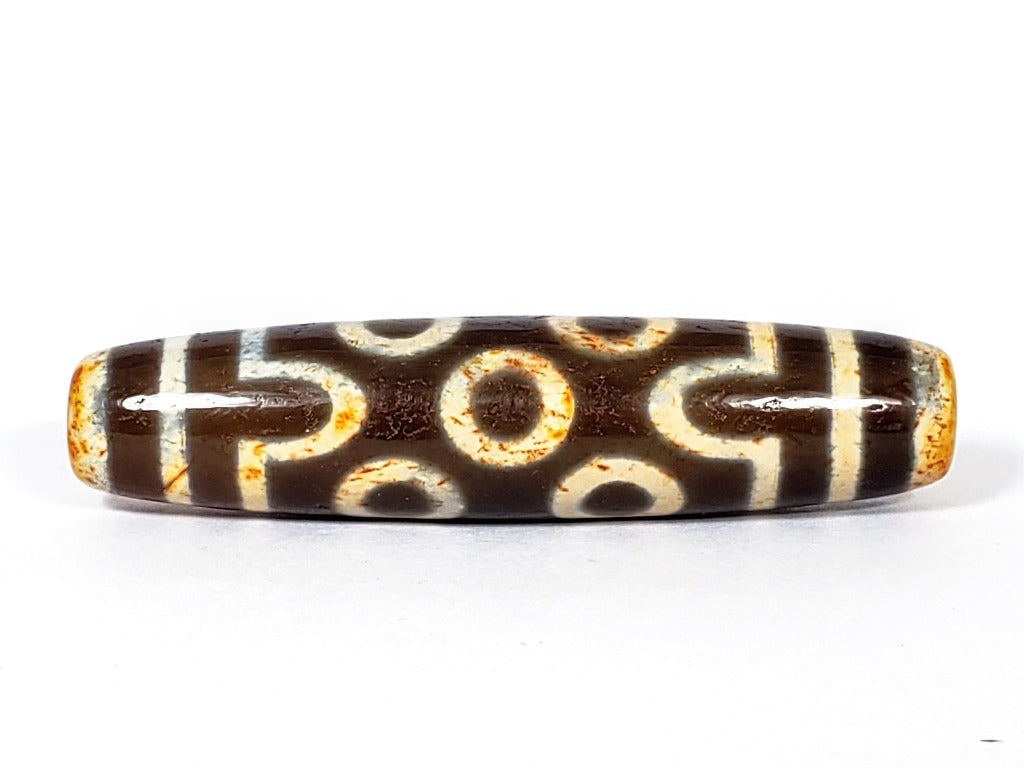 A vintage Dzi bead with a faux antique appearance featuring a captivating seven-eye motif. The bead showcases intricate carvings, with seven eyes symbolizing protection, intuition, and spiritual awakening