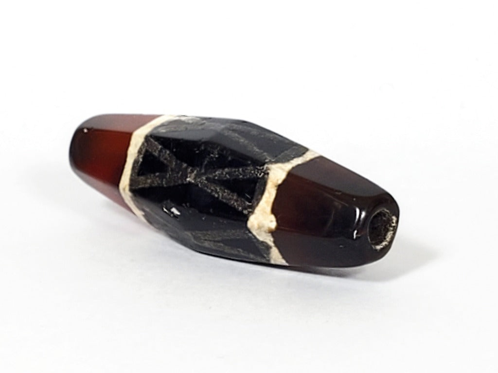 Authentic ancient Dzi bead featuring a captivating criss cross motif in vibrant carnelian. Its unique hexagon shape adds to its allure and historical significance.