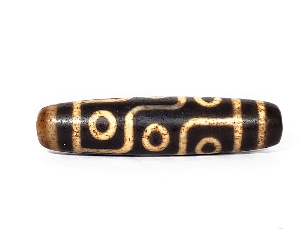 A vintage Dzi bead with a faux antique appearance featuring a mesmerizing nine-eye motif. The intricate details and weathered texture give it an aura of ancient wisdom and spirituality. 