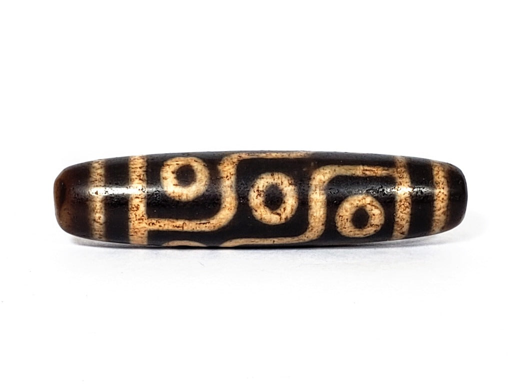 A vintage Dzi bead with a faux antique appearance featuring a captivating nine-eye motif. The intricate patterns and worn texture give it an ancient and mystical allure.