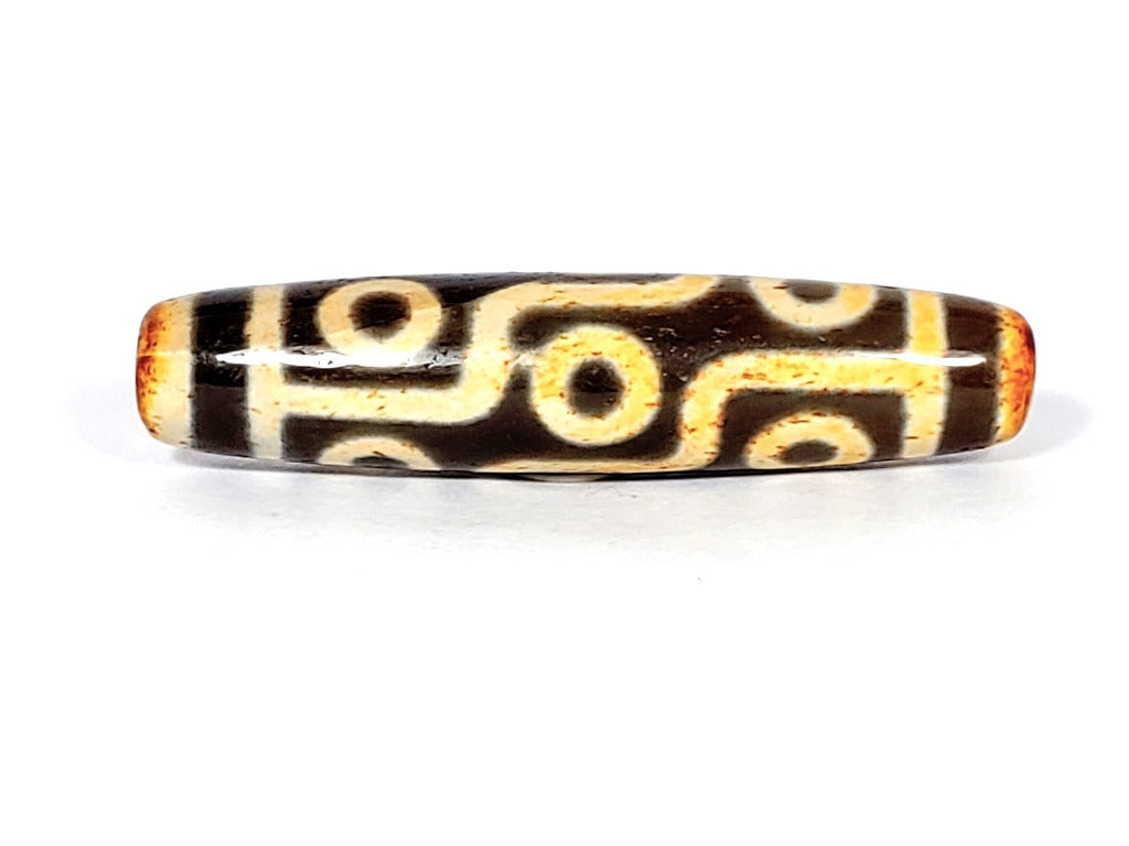 A vintage Dzi bead with a faux antique appearance featuring a captivating nine-eye motif. The bead showcases intricate carvings and a weathered texture, evoking a sense of ancient mystique and spiritual significance