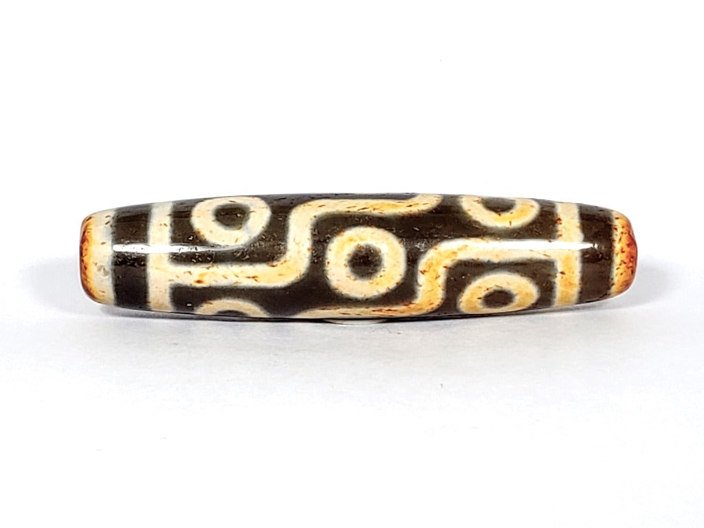 A vintage Dzi bead with a faux antique appearance featuring a captivating nine-eye motif. The bead showcases intricate carvings and a weathered texture, evoking a sense of ancient mystique and spiritual significance