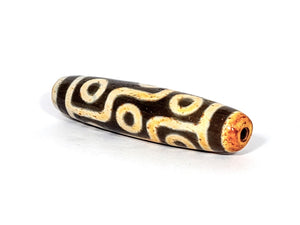 A vintage Dzi bead with a faux antique appearance featuring a captivating nine-eye motif. The bead showcases intricate carvings and a weathered texture, evoking a sense of ancient mystique and spiritual significance