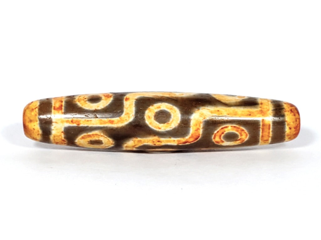 A vintage Dzi bead with a faux antique appearance featuring a mesmerizing nine-eye motif. The bead showcases intricate carvings, with nine eyes symbolizing protection, insight, and spiritual power. 