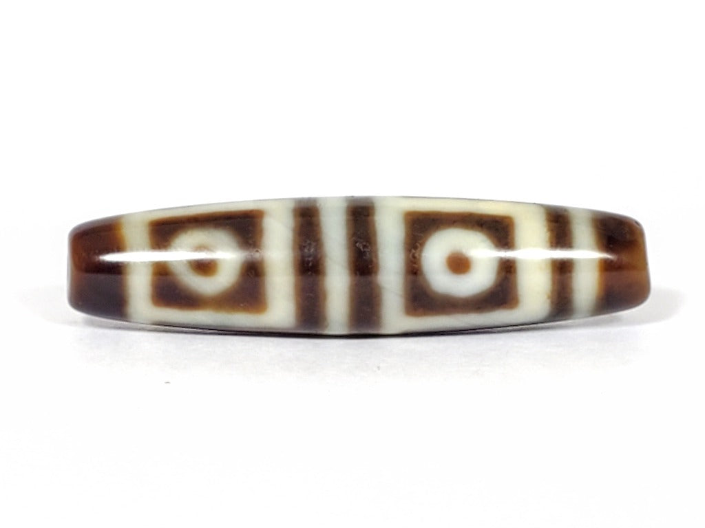 A vintage Dzi bead featuring a stunning Four Eye motif. The intricately carved eyes symbolize protection and spiritual insight. This exquisite bead is a prized collectible for Dzi bead enthusiasts.