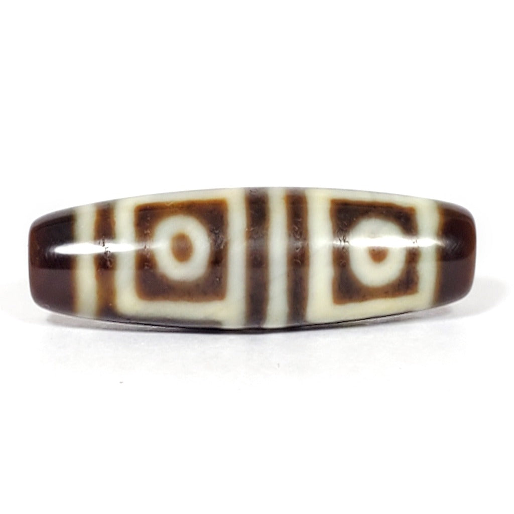 A vintage Dzi bead featuring a stunning Four Eye motif. The intricately carved eyes symbolize protection and spiritual insight. This exquisite bead is a prized collectible for Dzi bead enthusiasts.