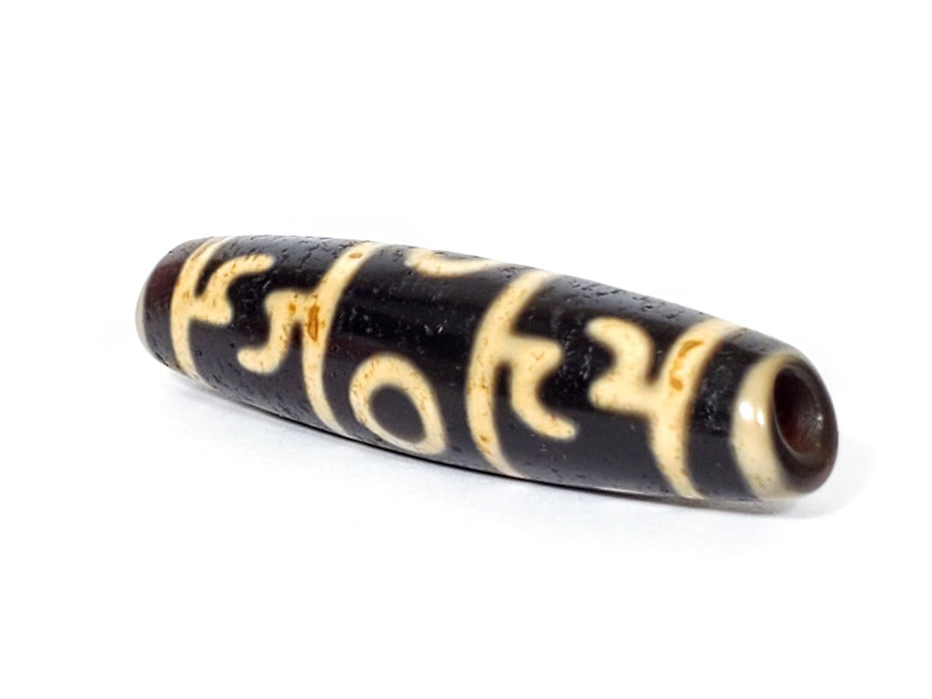 A vintage Dzi bead featuring the intricate Guru Rinpoche's Ritual Paraphernalia motif with a large keyhole drilling. This unique and rare artifact embodies the spiritual significance and artistic craftsmanship of Dzi beads