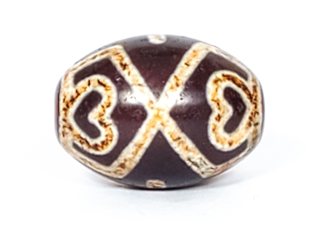 A vintage Dzi bead featuring a round shape adorned with a captivating Four Eye Lotus & Cross motif. This authentic artifact, identified as R-FoELC, showcases the intricate patterns and spiritual symbolism of ancient Dzi beads