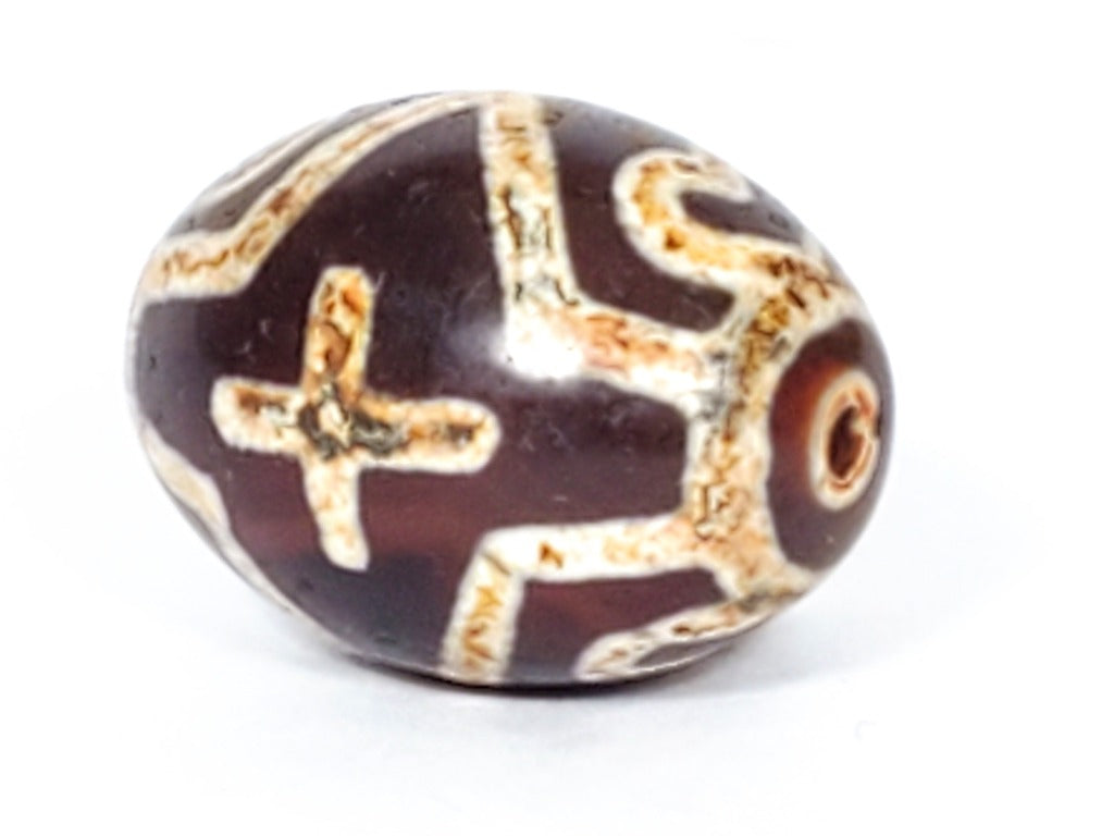 A vintage Dzi bead featuring a round shape adorned with a captivating Four Eye Lotus & Cross motif. This authentic artifact, identified as R-FoELC, showcases the intricate patterns and spiritual symbolism of ancient Dzi beads