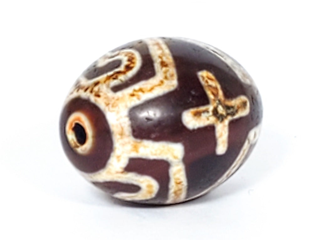 A vintage Dzi bead featuring a round shape adorned with a captivating Four Eye Lotus & Cross motif. This authentic artifact, identified as R-FoELC, showcases the intricate patterns and spiritual symbolism of ancient Dzi beads