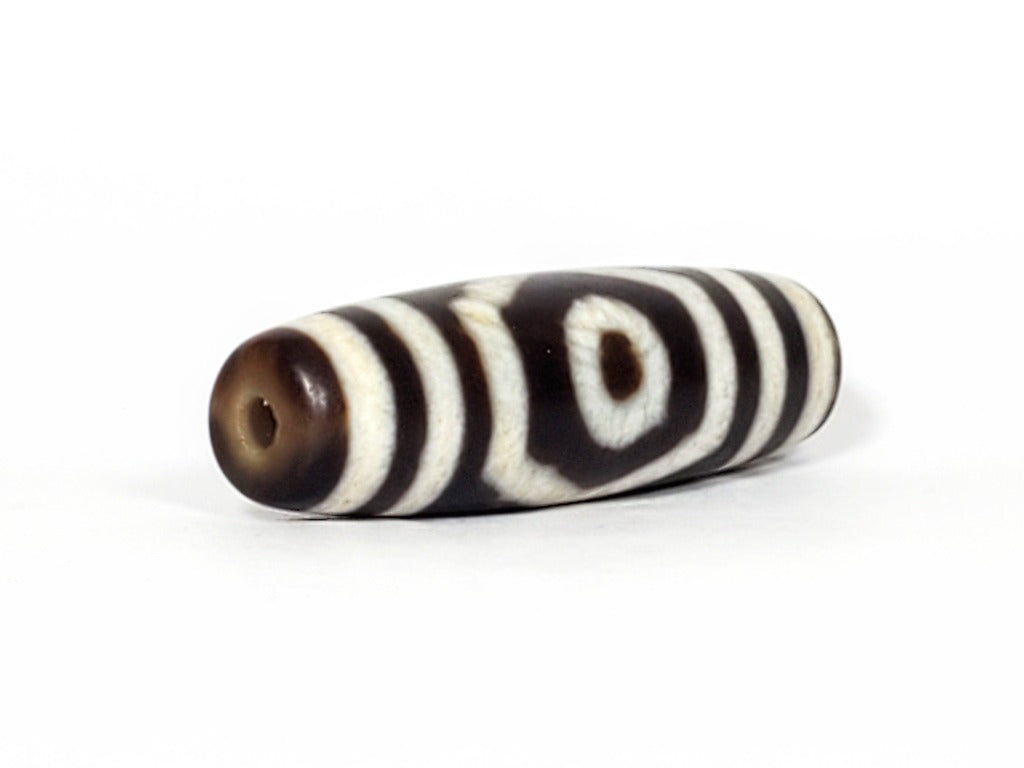 A vintage Dzi bead featuring a mesmerizing Three Eye Motif. This authentic artifact, identified as TaD-ThE-1, showcases the intricate craftsmanship and spiritual significance of ancient Dzi beads