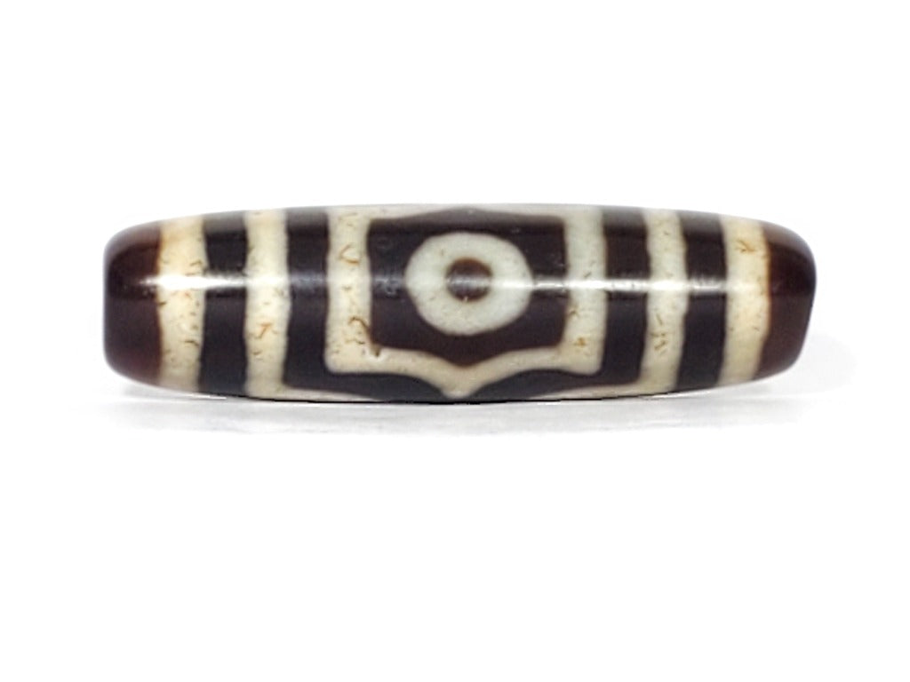 A vintage Dzi bead featuring a rare triangular shape and a captivating Three Eye Motif. This authentic artifact showcases the unique design and spiritual symbolism of ancient Dzi beads