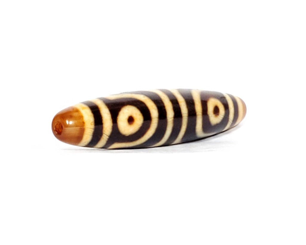 ancient Dzi bead adorned with a powerful Four Eye & Tiger Tooth motif. This bead carries deep spiritual symbolism, representing enhanced perception, inner strength, and protection. The Four Eye motif symbolizes heightened spiritual vision, while the Tiger Tooth motif embodies courage and warding off negative energies