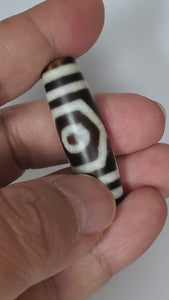 A vintage Dzi bead featuring a mesmerizing Three Eye Motif. This authentic artifact, identified as TaD-ThE-1, showcases the intricate craftsmanship and spiritual significance of ancient Dzi beads