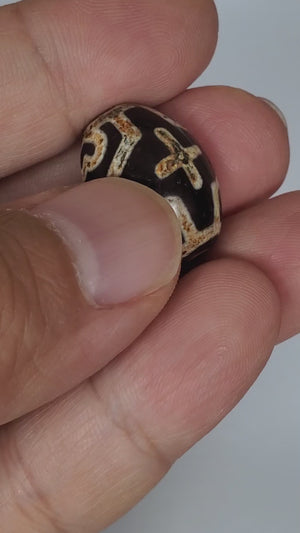 A vintage Dzi bead featuring a round shape adorned with a captivating Four Eye Lotus & Cross motif. This authentic artifact, identified as R-FoELC, showcases the intricate patterns and spiritual symbolism of ancient Dzi beads